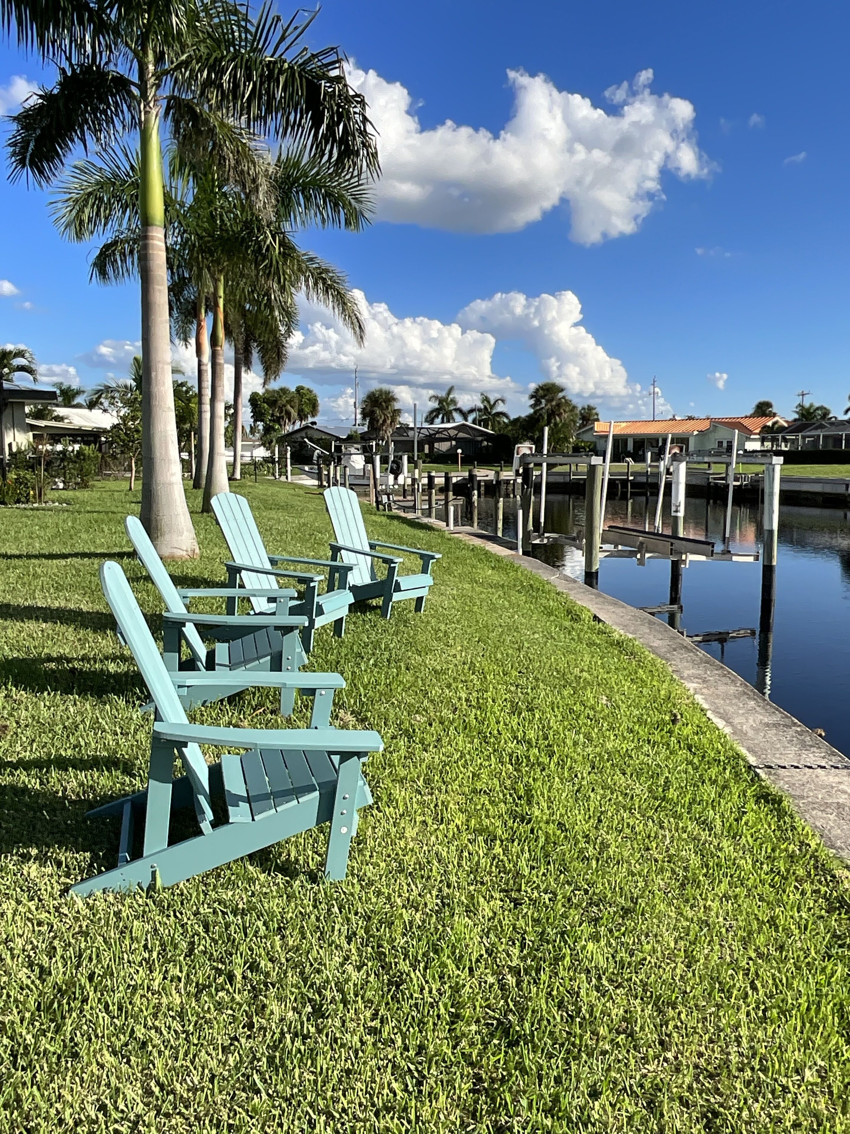 A grassy area with three light blue Adirondack chairs and a body of water with docks.