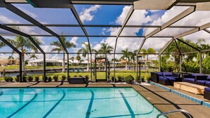 A pool area with a view of palm trees and houses, a covered seating area with blue cushions, and a clear blue pool. -  BRING YOUR SAIL BOAT  (Punta Gorda)