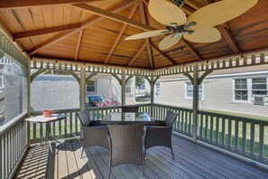 Une terrasse extérieure couverte, équipée d’une table et de chaises, d’un ventilateur de plafond et offrant une vue sur les maisons voisines.