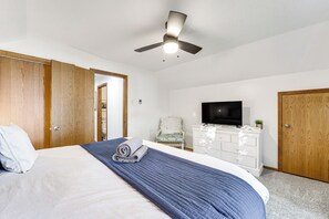 A bedroom with a bed, a ceiling fan, a TV, a dresser, and wooden doors. - Scenic Cottage w/ Private Dock on Torch Lake (Central Lake)