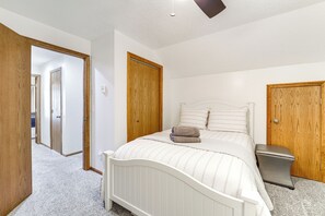 Un dormitorio con cama, puerta de madera y ventilador de techo blanco.