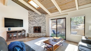 A living room with a stone fireplace, a flat-screen TV, a wooden ceiling, and a sliding glass door leading to an outdoor area. - Stylish Incline Village Vacation Rental w/ A/c! (Incline Village)