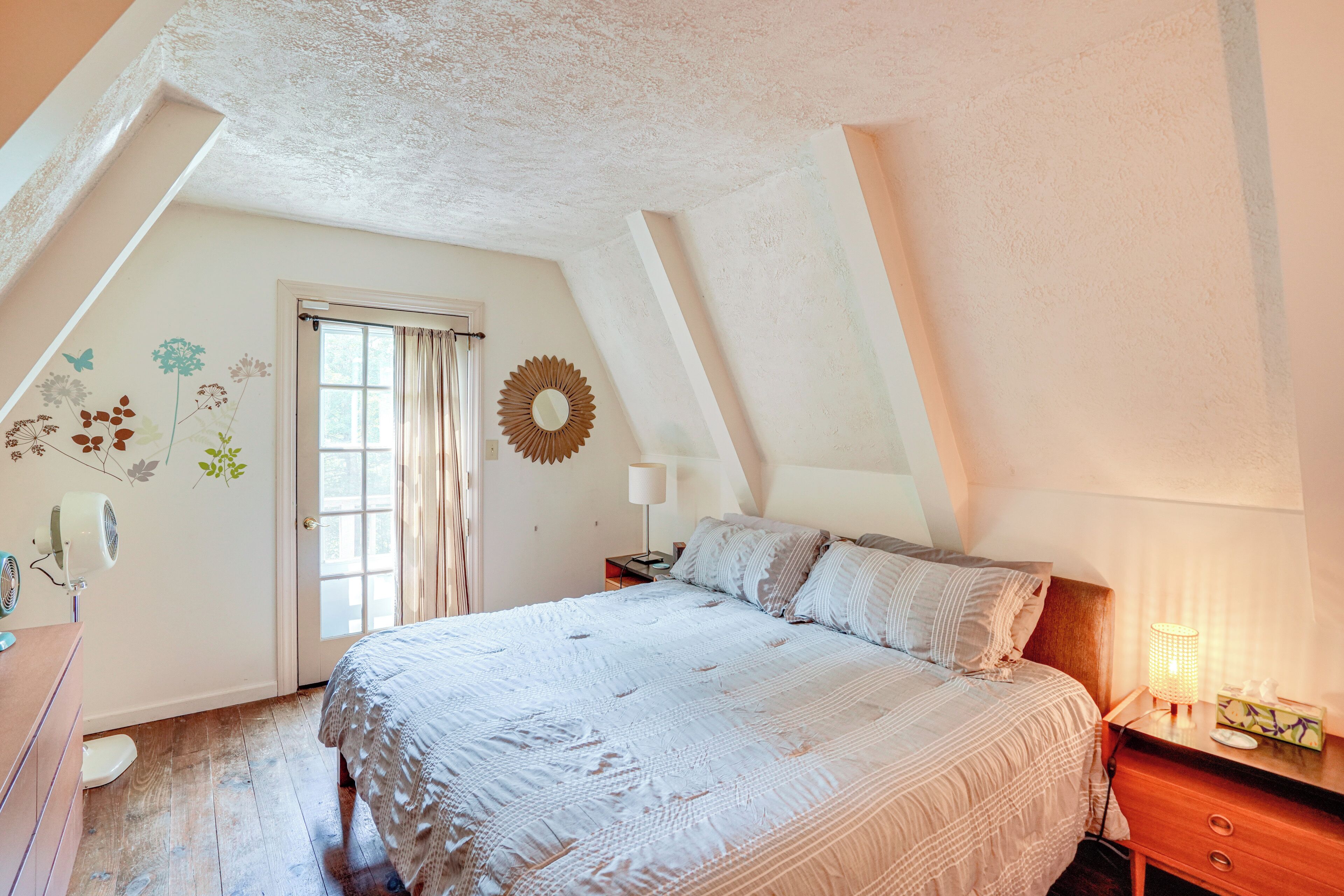 Een slaapkamer met een groot bed, een nachtkastje, een dressoir, een raam met gordijnen en een decoratie aan de muur.
