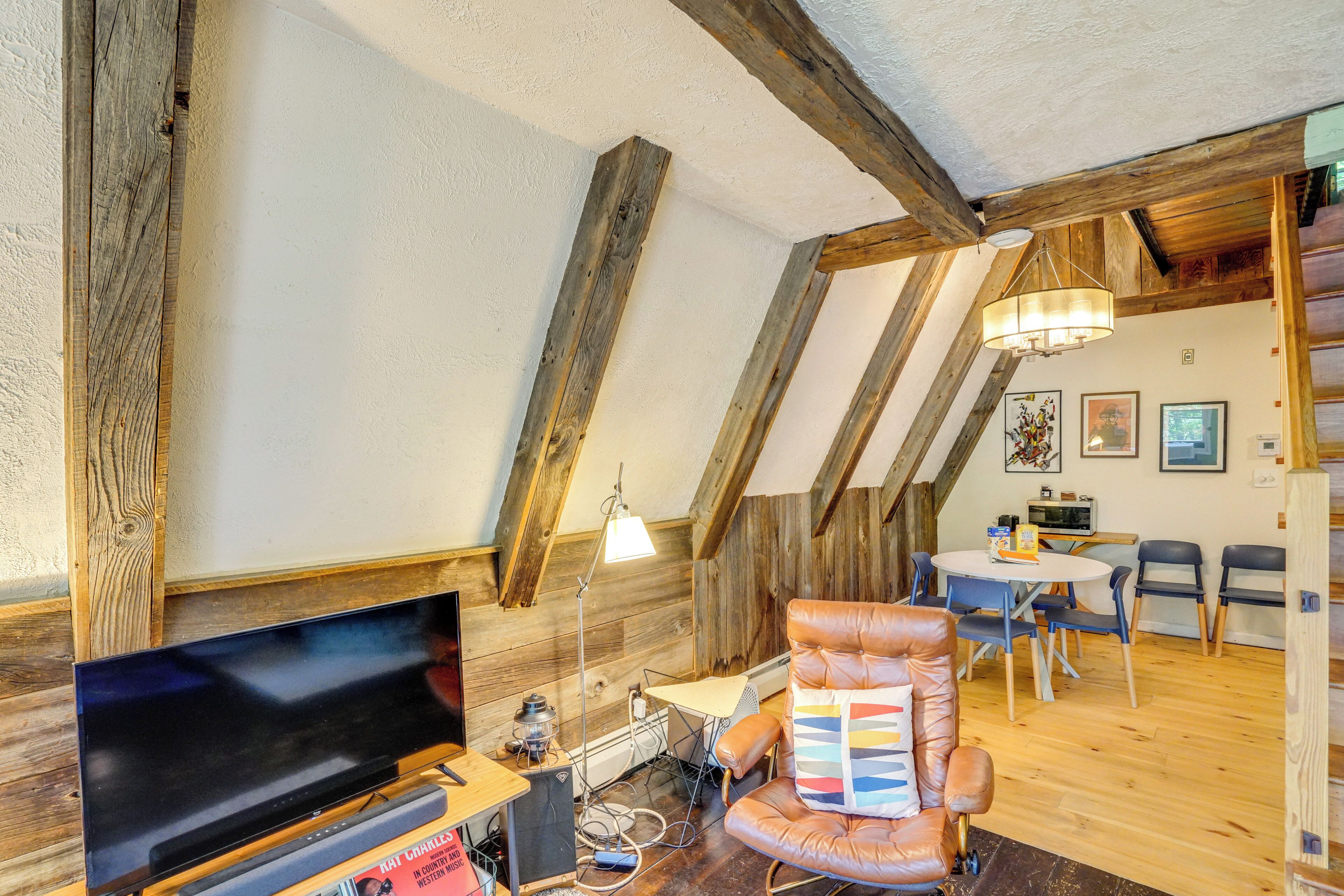 Un dormitorio estilo loft con vigas de madera a la vista, televisor, sillón de cuero, mesa de comedor con sillas y una araña.