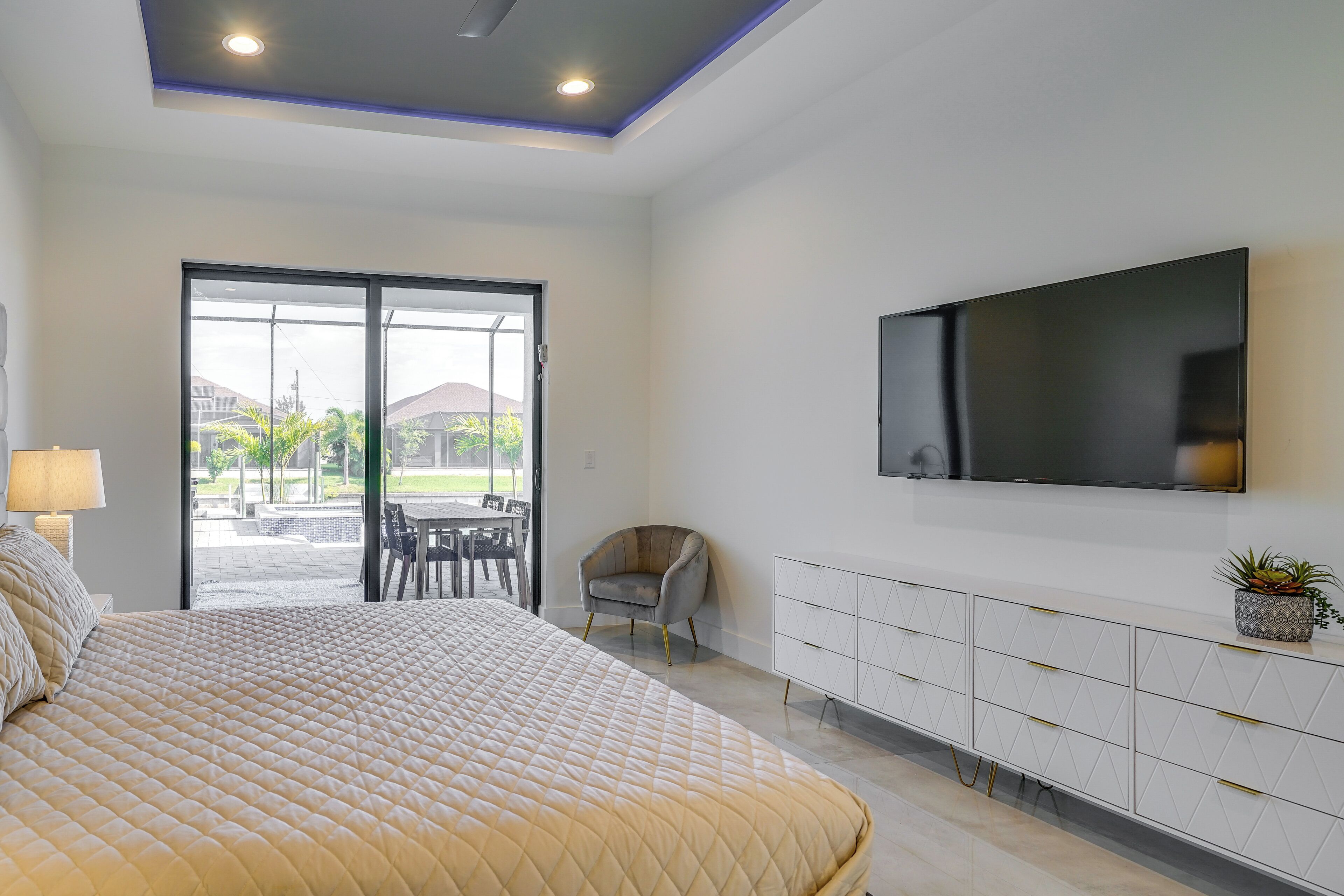 A bedroom with a large bed, a TV mounted on the wall, a chair, and a sliding glass door leading to an outdoor area.