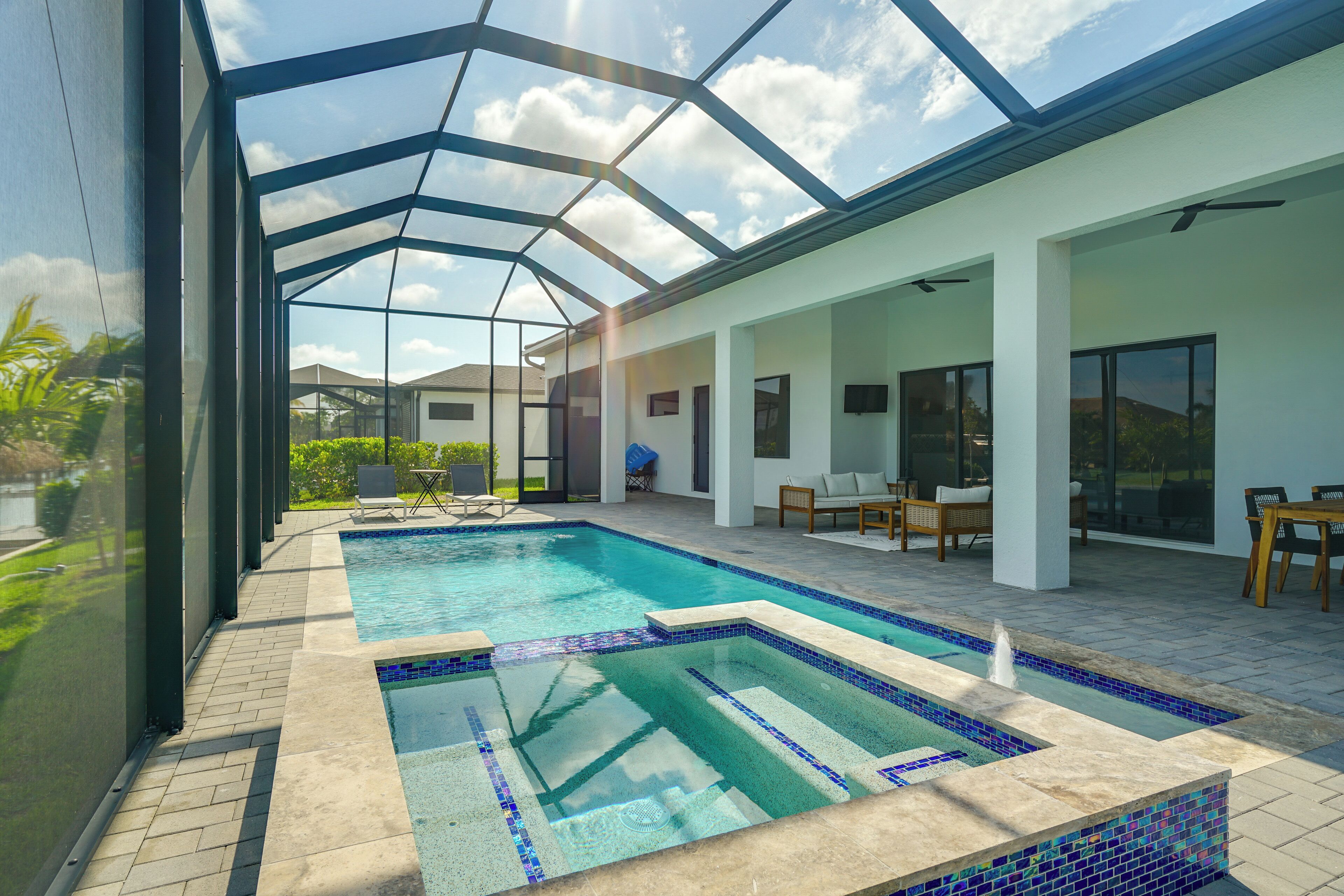 An indoor swimming pool with a glass ceiling, surrounded by seating areas and a patio.