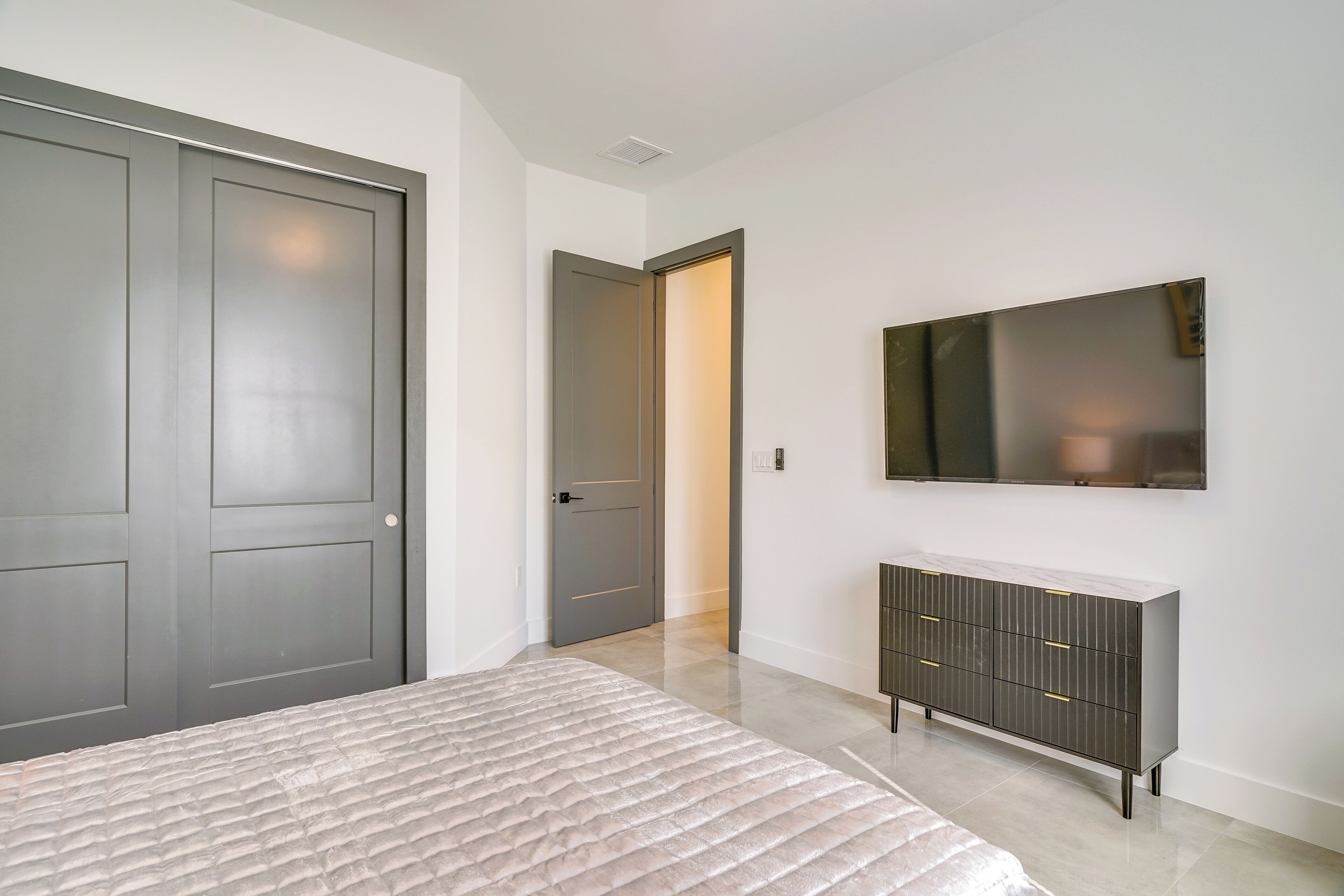 Un dormitorio con una cama, un tocador, un televisor y una puerta que da a otra habitación.