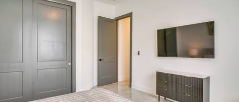Un dormitorio con una cama, un tocador, un televisor y una puerta que da a otra habitación.