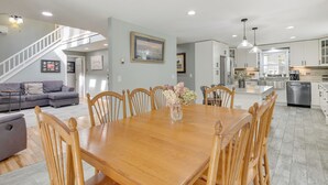 A spacious living area with a wooden dining table, a gray sofa, and a staircase leading to an upper level. - Searsport Paradise w/ Private Pool & Patio! (Searsport)