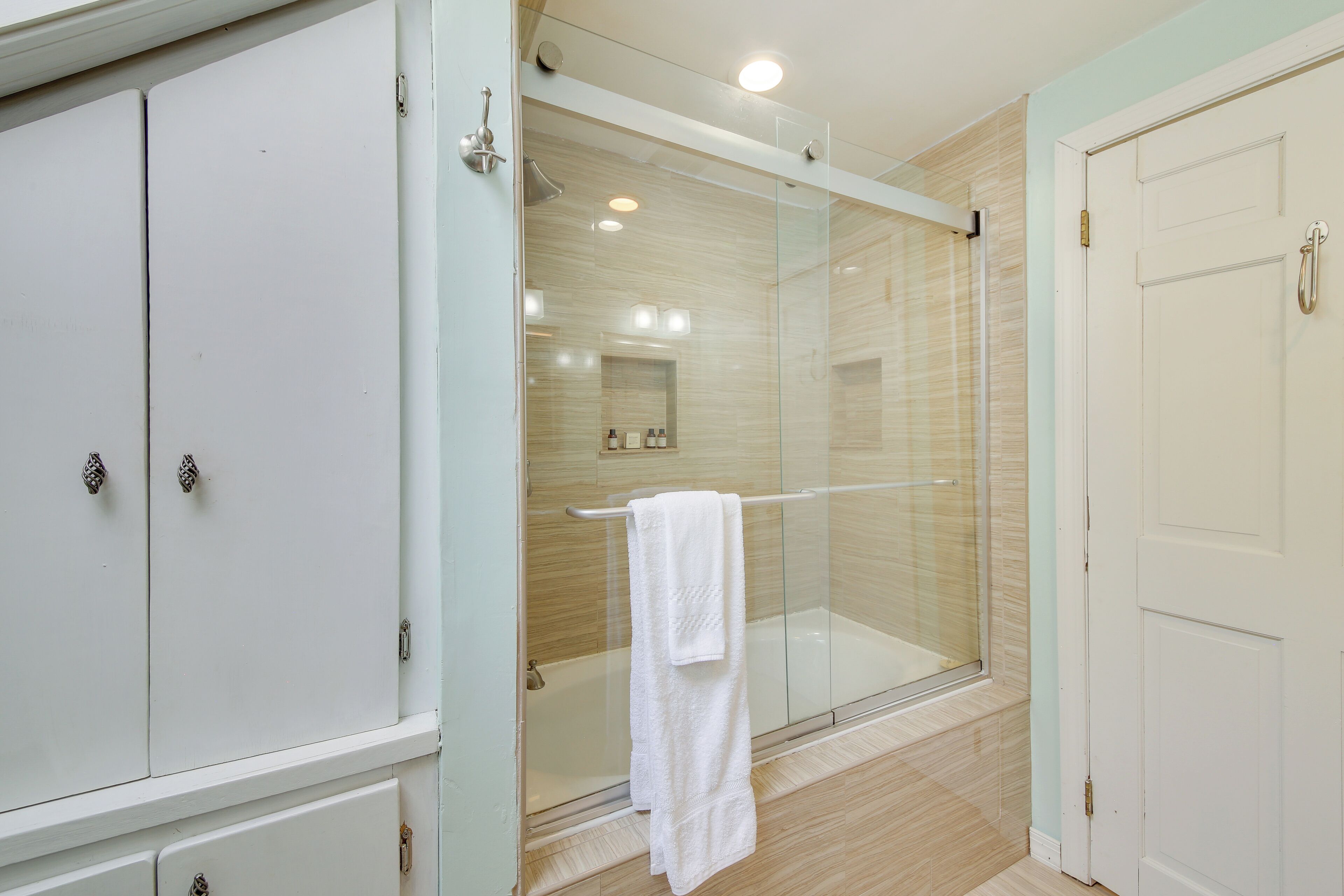 Un baño con cabina de ducha de vidrio, una toalla blanca colgada en un perchero y una puerta blanca.