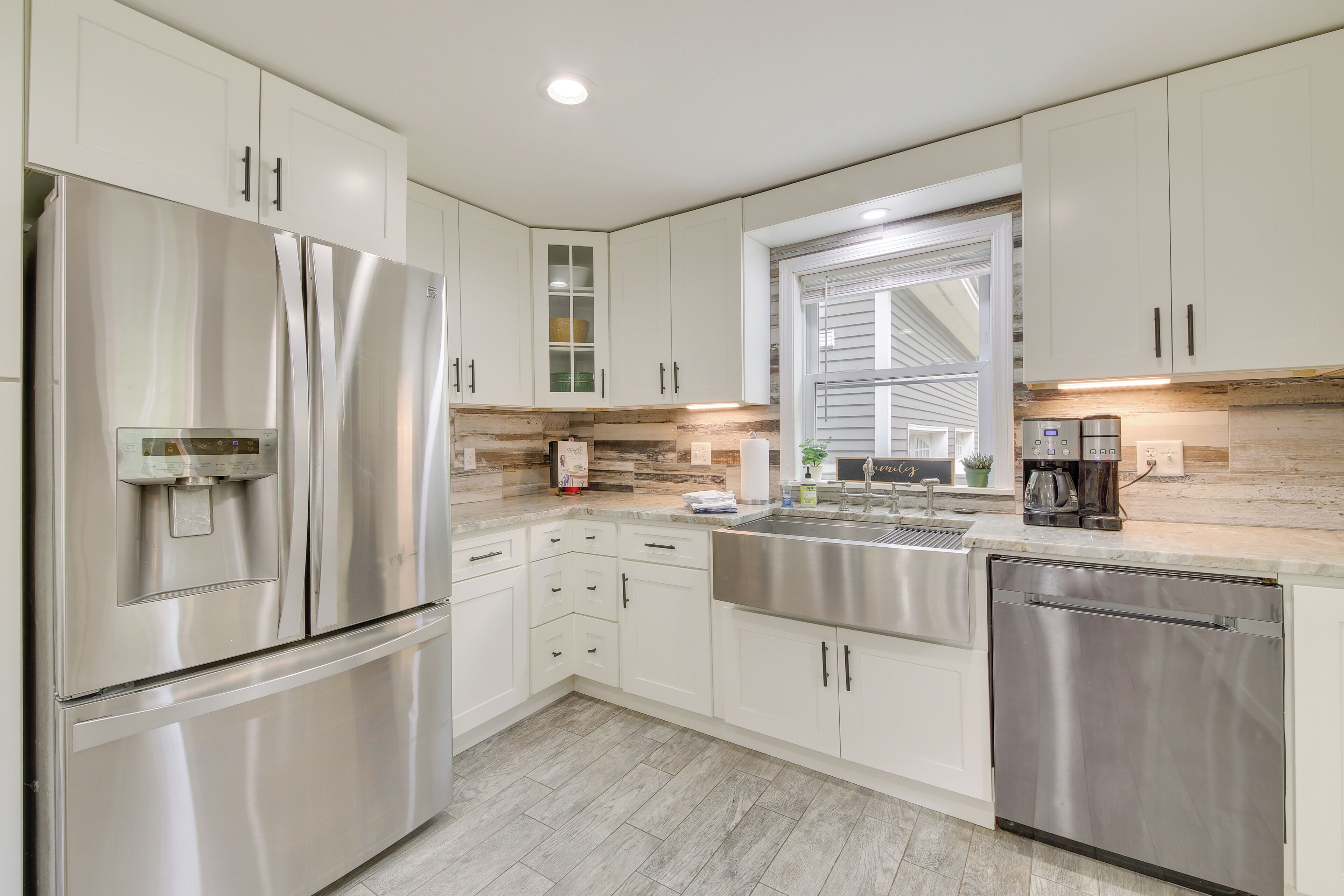 A modern kitchen with stainless steel appliances, white cabinetry, a window, and a built-in coffee maker.