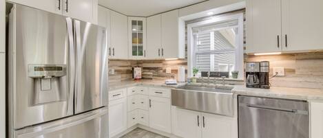 A modern kitchen with stainless steel appliances, white cabinetry, a window, and a built-in coffee maker.