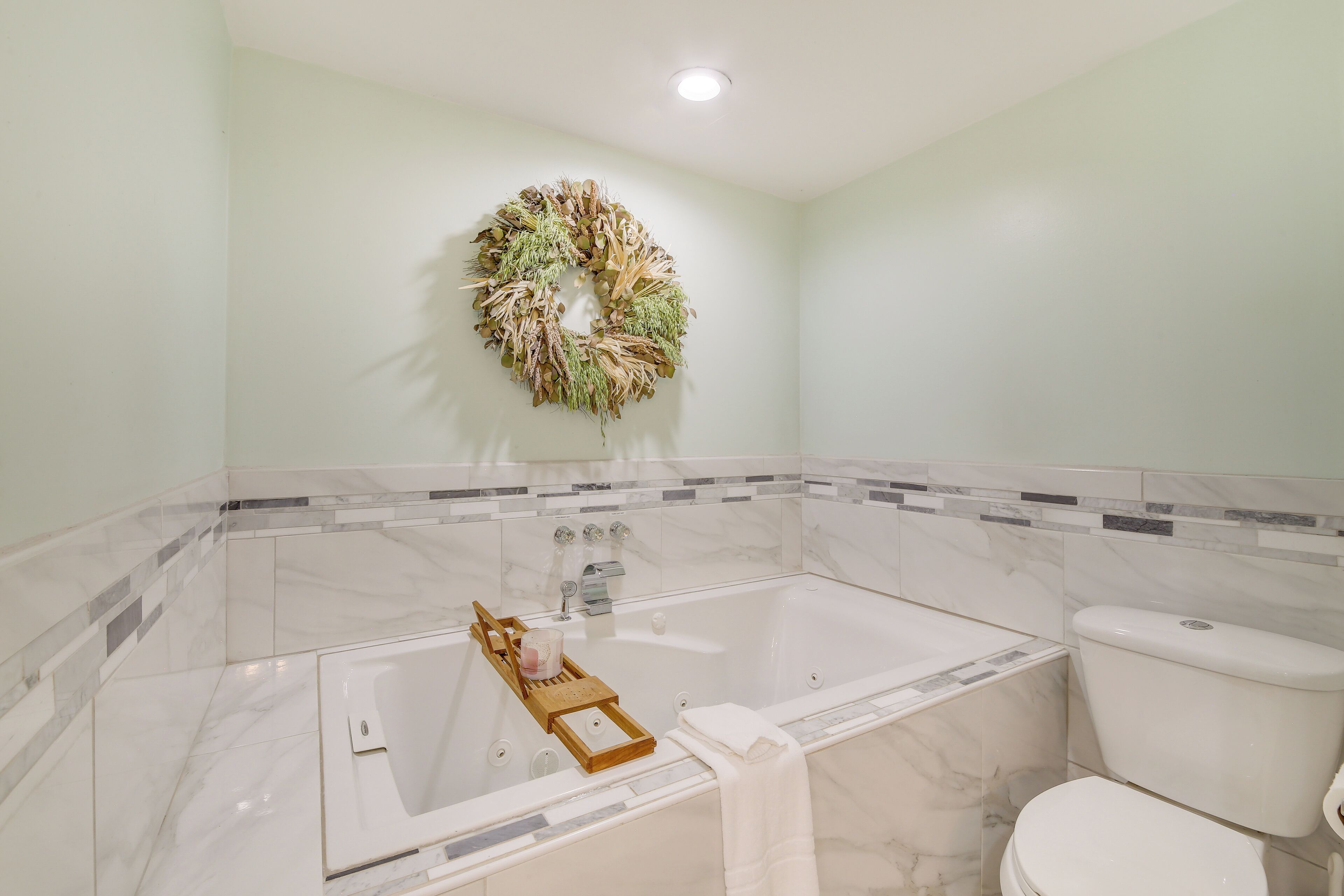 A bathroom with a bathtub, toilet, and a decorative wreath on the wall.