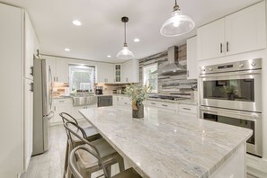 A modern kitchen with white cabinetry, stainless steel appliances, a marble island, and pendant lighting. - Searsport Paradise w/ Private Pool & Patio! (Searsport)