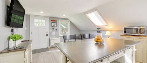 A modern kitchen with a large island, a flat-screen TV, and a microwave.