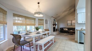 Une cuisine spacieuse avec des meubles blancs, un coin repas avec une table et un banc blancs, et un salon confortable avec un canapé et une cheminée.