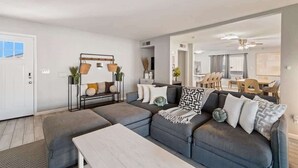 Een moderne woonkamer met een hoekbank, een salontafel en een eethoek op de achtergrond.