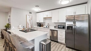 Een moderne keuken met witte kasten, roestvrijstalen apparatuur, een centraal eiland met barkrukken en een vaatwasser.