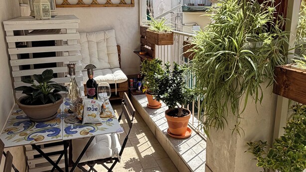 Un petit balcon avec une table, des chaises, des plantes en pot et une vue sur les immeubles.