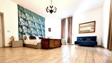 A modern bedroom with a large bed, a dresser, a blue sofa, a chandelier, and a large mirror.