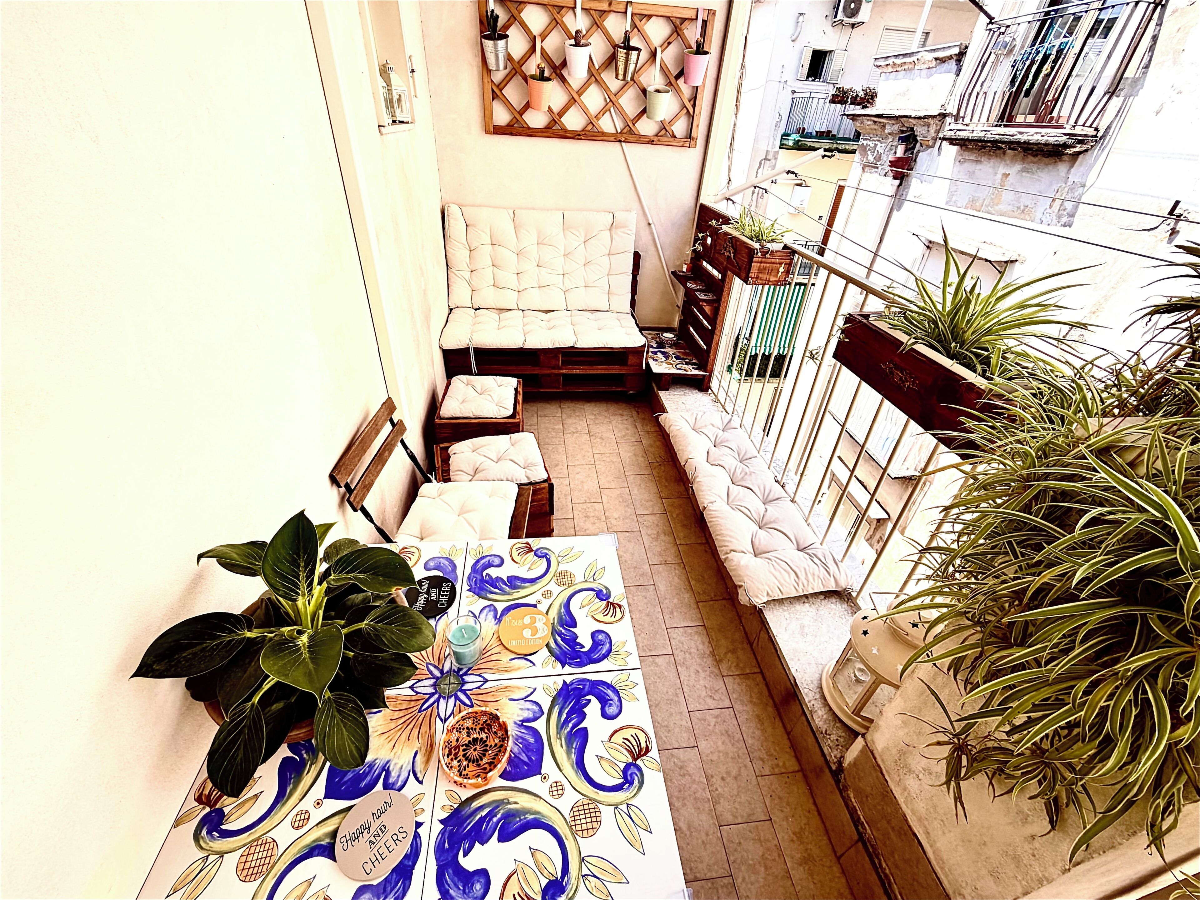 A narrow balcony with a table, chairs, and potted plants.