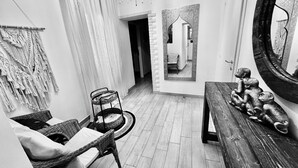 Un couloir avec un fauteuil en osier, une petite table et un miroir orné de sculptures de singes.