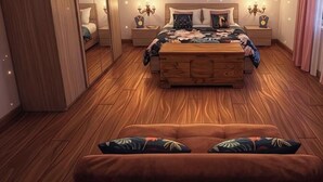 Une chambre avec un plancher en bois, un lit recouvert d’une couvre-lit à motifs floraux, une table de chevet avec une lampe et une commode avec une horloge.