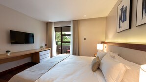 Habitación de hotel con una cama grande, televisión de pantalla plana, escritorio y balcón con una silla.