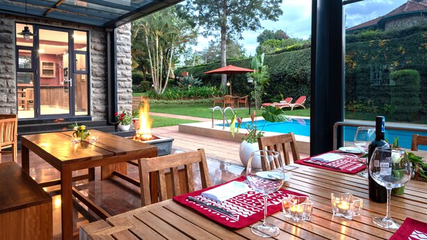 Un comedor con mesas y sillas de madera, una piscina y vistas al jardín.
