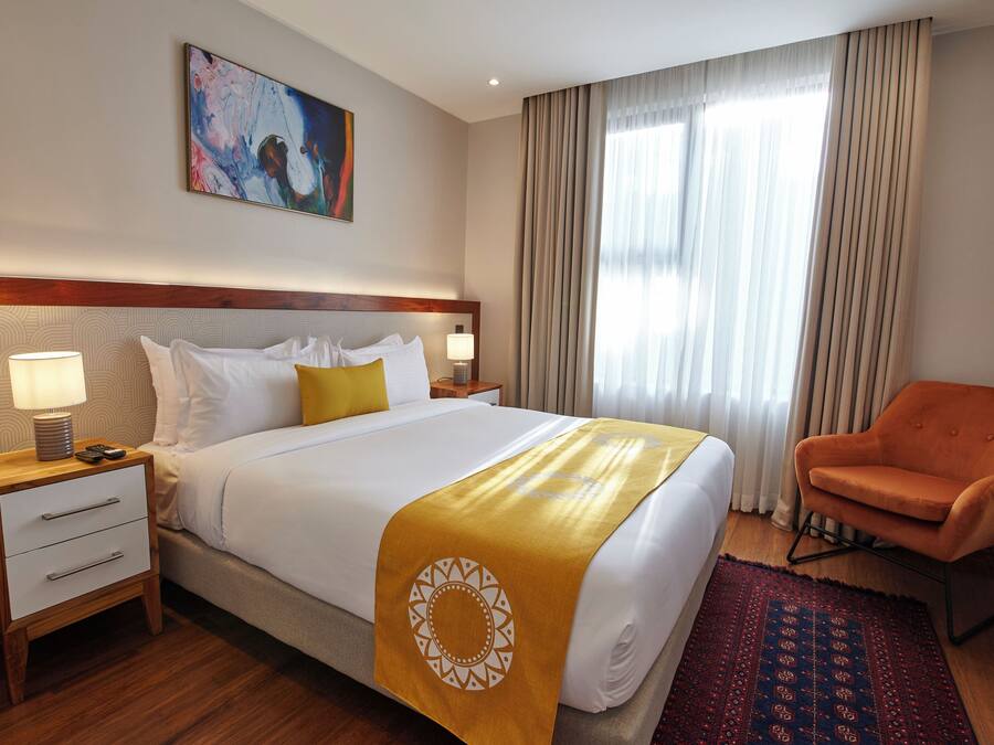 A hotel room with a large bed, a nightstand, a chair, and a painting on the wall.