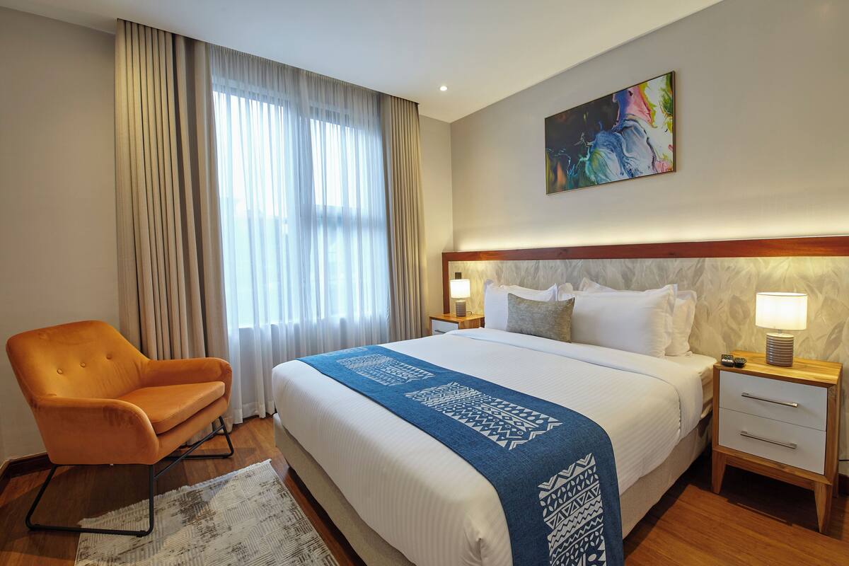 Een hotelkamer met een groot bed, een stoel, een nachtkastje met een lamp en een schilderij aan de muur.