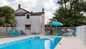 A swimming pool with lounge chairs and an umbrella, surrounded by a white fence and a white building. - Maison de Campagne "monplaisir" en Quercy Blanc (Montlauzun)