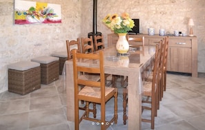 Un comedor con una larga mesa de madera, sillas de mimbre y un jarrón con flores.