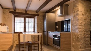A kitchen with a wooden table and chairs, a refrigerator, an oven, and a window with blinds. - Maison de Campagne "monplaisir" en Quercy Blanc (Montlauzun)