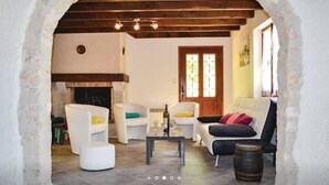 A cozy living room with a fireplace, white sofas, a coffee table, and a rustic stone archway. - Maison de Campagne "monplaisir" en Quercy Blanc (Montlauzun)