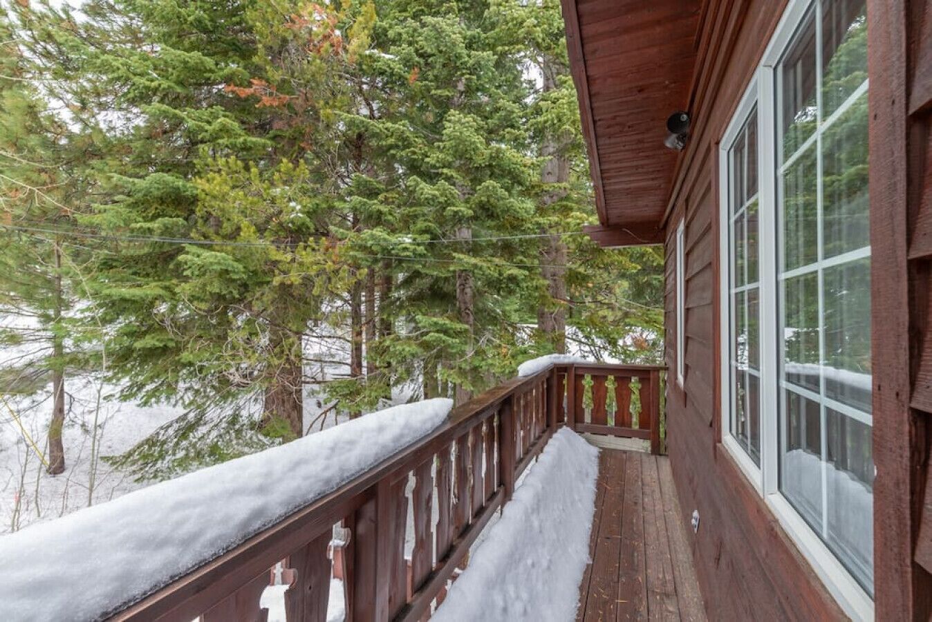A wooden deck with snow-covered railings and a large window.