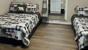 Un dormitorio con dos camas, una mesita de noche, una lámpara de pie y un baño visible a través de una puerta abierta.