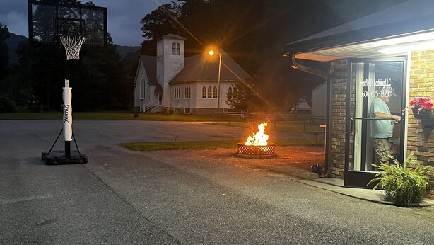 Una cancha de baloncesto con aro, un pequeño pozo de fuego y un edificio con fachada de ladrillo.