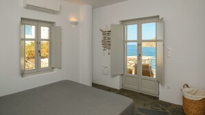 A room with a bed, two windows, a wall-mounted air conditioner, and a view of the beach. - Amorgos Elegant Houses, Villa 2 (Amorgos)