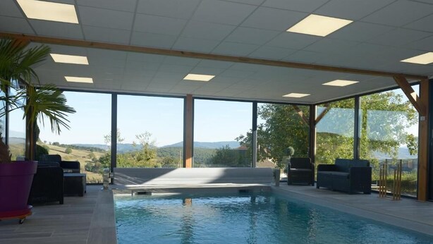 Una piscina interior con vistas despejadas al exterior, rodeada de zonas de estar y plantas en macetas.