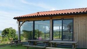 Un edificio de madera con techo de tejas rojas y amplios ventanales. Hay dos mesas de picnic afuera.