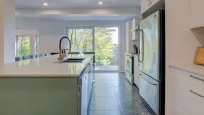 Cozinha moderna com uma ilha grande, eletrodomésticos de aço inoxidável e vista para o exterior.