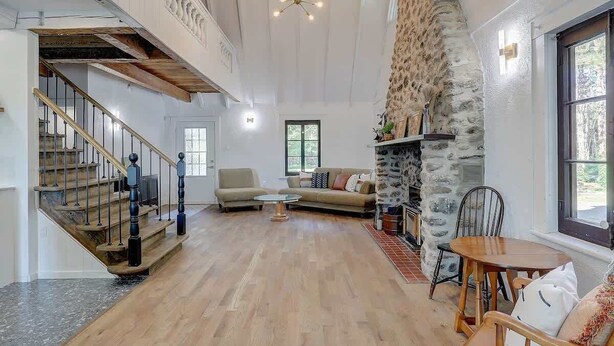 Uma sala de estar ampla com escada de madeira, parede de pedra e lareira.