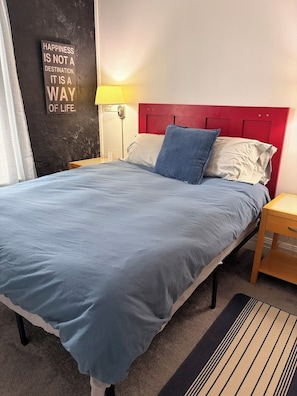 Ein Bett mit blauer Bettdecke, einem roten Kopfteil und einer Wand mit einem motivierenden Zitat.