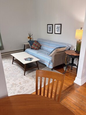 A cozy living room with a sofa, a coffee table, a wooden chair, a small side table, and a lamp.