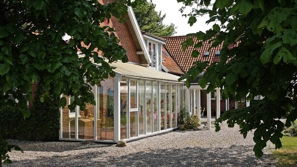 Une véranda dotée d’un toit en verre, entourée d’une allée gravillonnée et d’une maison en briques avec un toit en tuiles.