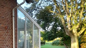 Une maison avec une allée en gravier, un grand arbre et une véranda en verre.