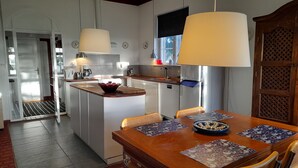 Une cuisine moderne avec des meubles blancs, un îlot central en bois et un coin repas comprenant une table et des chaises en bois.