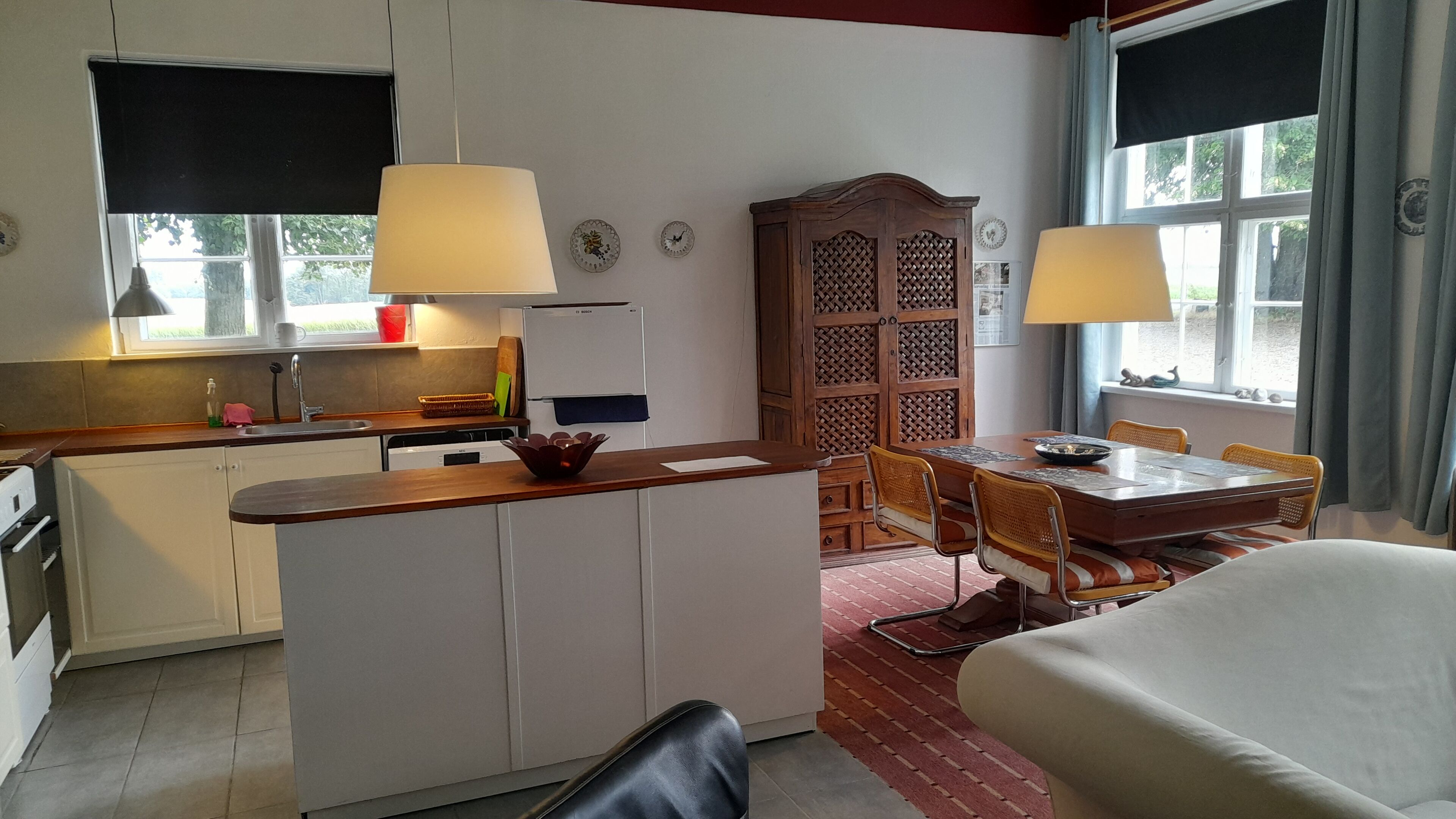 A compact kitchen with a dining area, a refrigerator, and a window with curtains.