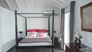 Una cama con dosel de cuatro postes con acabado oscuro, una mesita de noche con lámpara y un cuadro enmarcado en la pared.